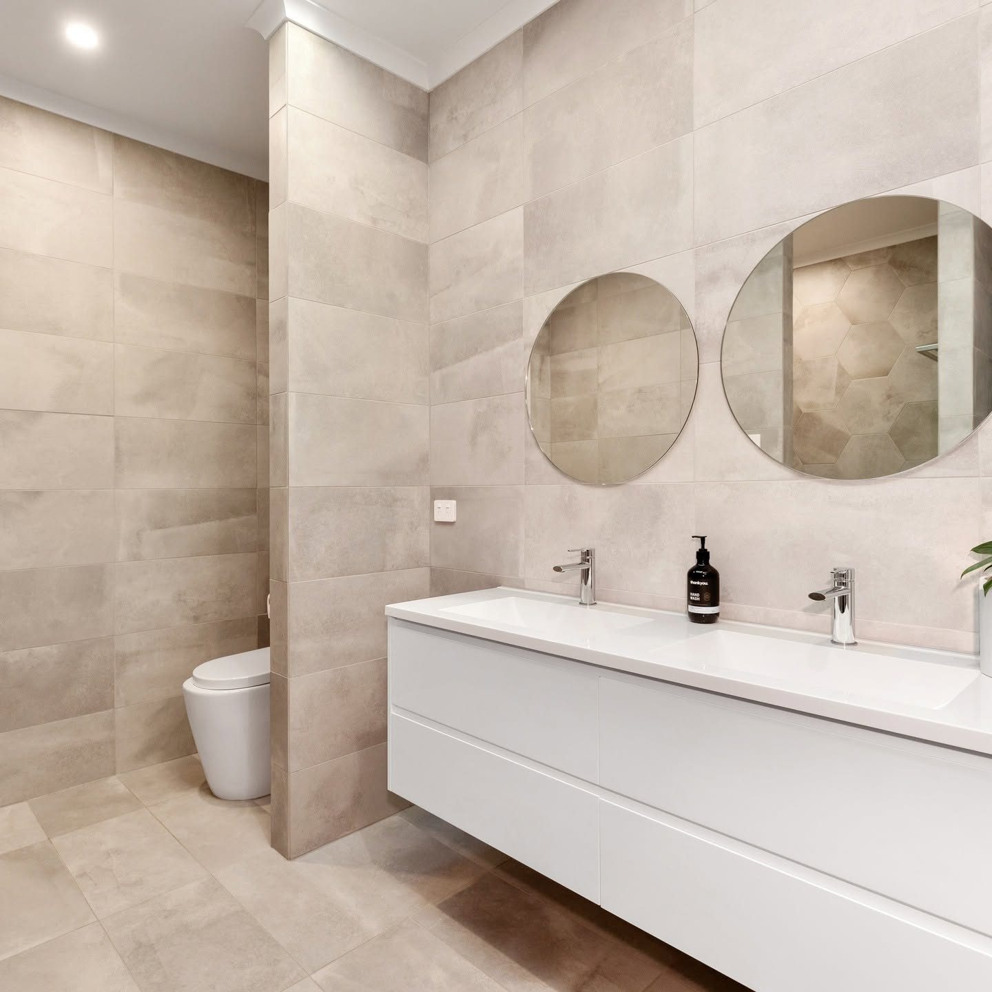 Renovated bathroom with large-format tiles and twin round mirrors